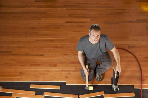 Floorman manually adjusting and installing wood flooring